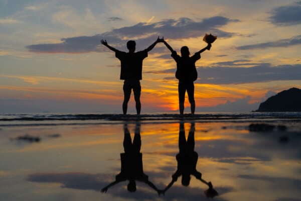 浜辺で夕陽を眺めるカップル