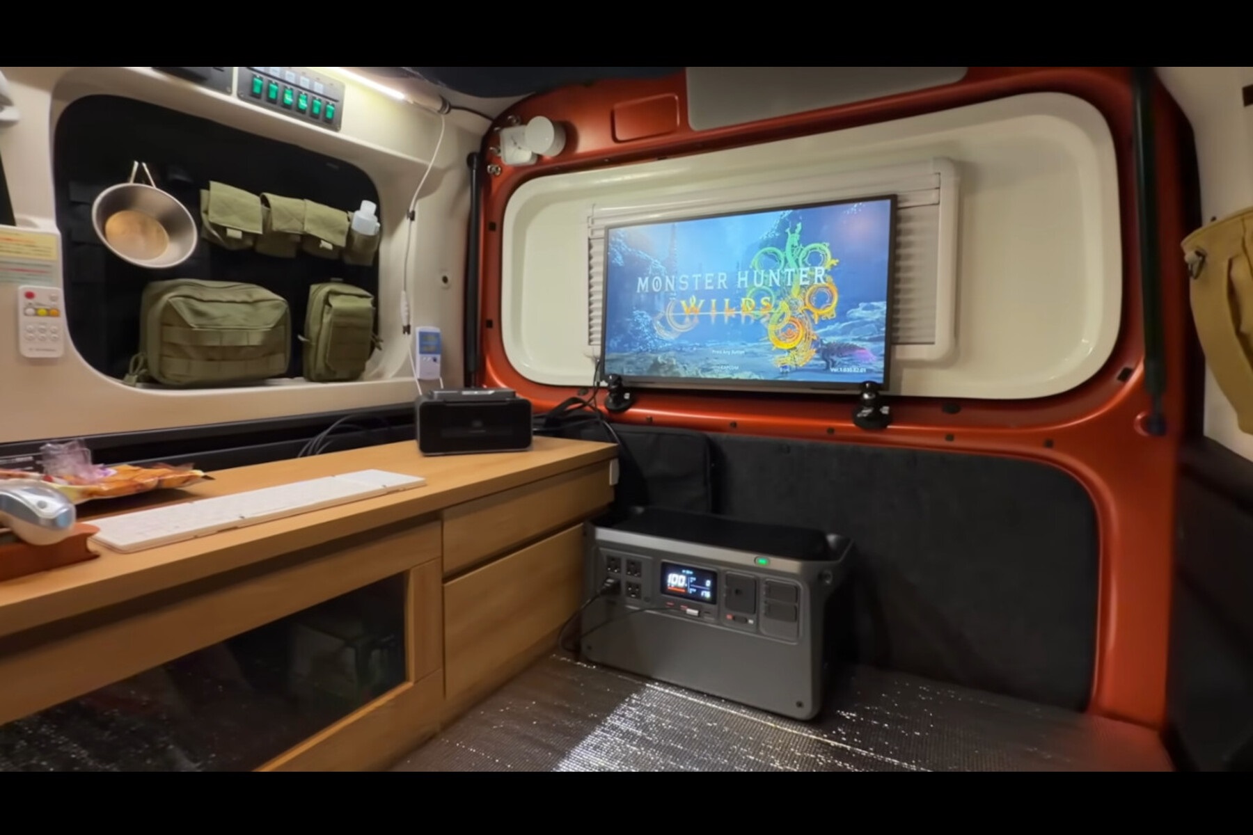 Dentanさんの愛車ダイハツ・アトレーの車内に構築したゲーム環境。マグネット製の支柱を2本取付、バックドアを背にモニターを立てかけ、マグネットタイプのポータブルスピーカーをドア上部に取り付け。ポータブル電源で給電しながらゲームします。